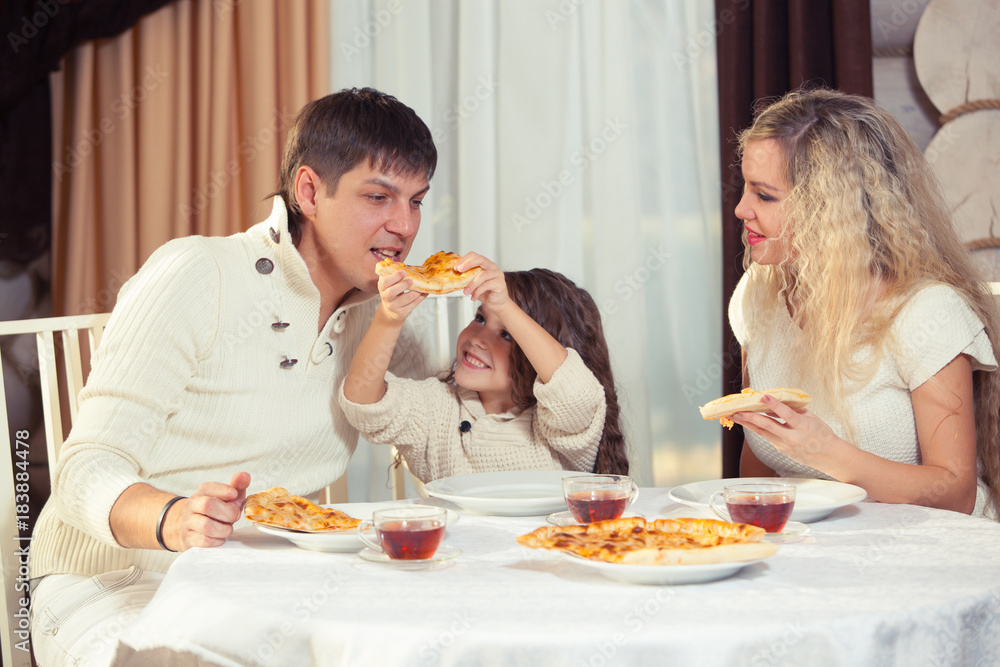 Family eating dinner at a dining table, Round table, pizza, orange, house made of wood Family eating dinner at a dining table, Round table, pizza, orange, house made of wood