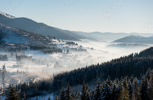 Winter morning landscape. The first shadows of raising sun on mountain slopes, ski resort in a white haze