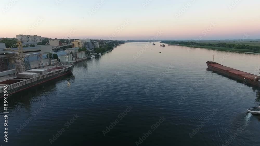 A striking view of the wide Dnipro with a floating big barge, a turning white steamship, and impressive embankment at a splendid sunset. A striking view of the wide Dnipro with a floating big barge, a turning white steamship, and impressive embankment at a splendid sunset.