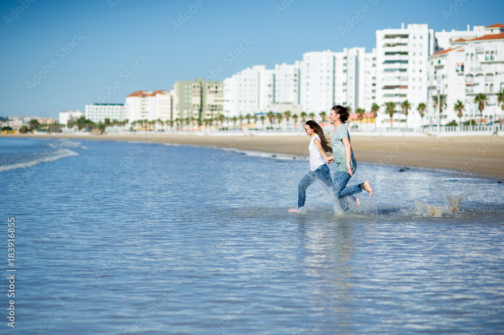 The young couple runs in the sea, raising splashes.