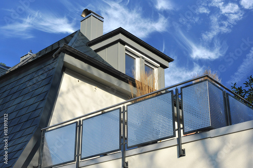 Edelstahlbalkon, mit rechteckigen schwarzen Kunststoffschindeln neu eingedecktes Dach mit metall-verkleideter Gaube und Schornstein mit Edelstahl-Kragen/-Dach und modernem Schneefang photo