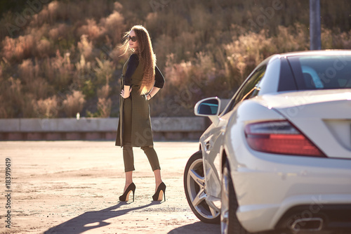 beautiful business woman in sunglasses and business suit at sunset on the background of an expensive car