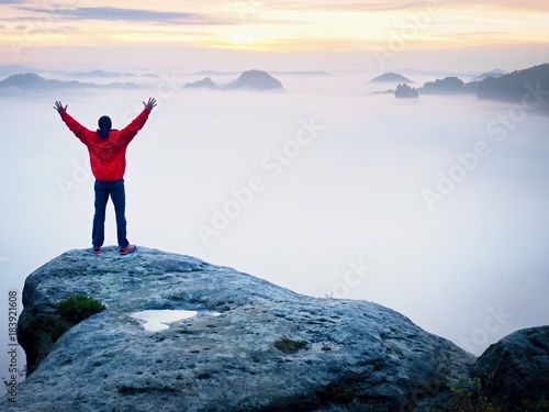 Tall tourist celebrate on the peak of the world . Orange thick fog bellow in deep valley. Dreamy daybreak