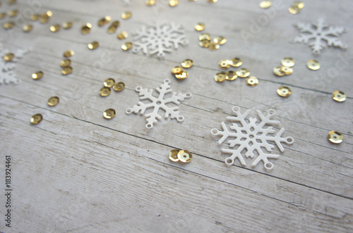 White paper snowflakes and gold sequins on light wooden background with copy space, christmas and new year, minimalistic design