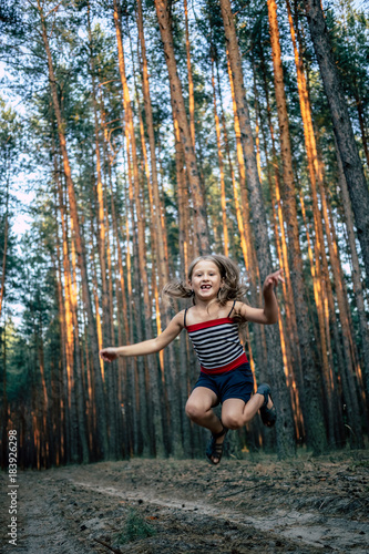 Beautiful little girl in the pine forest in summer.