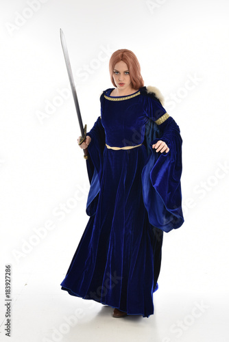  full length portrait of girl wearing long blue velvet gown and fur lined cloak, standing pose  on white background. © faestock