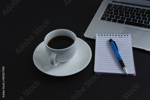 Black coffee, pen, notepad and laptop on black background