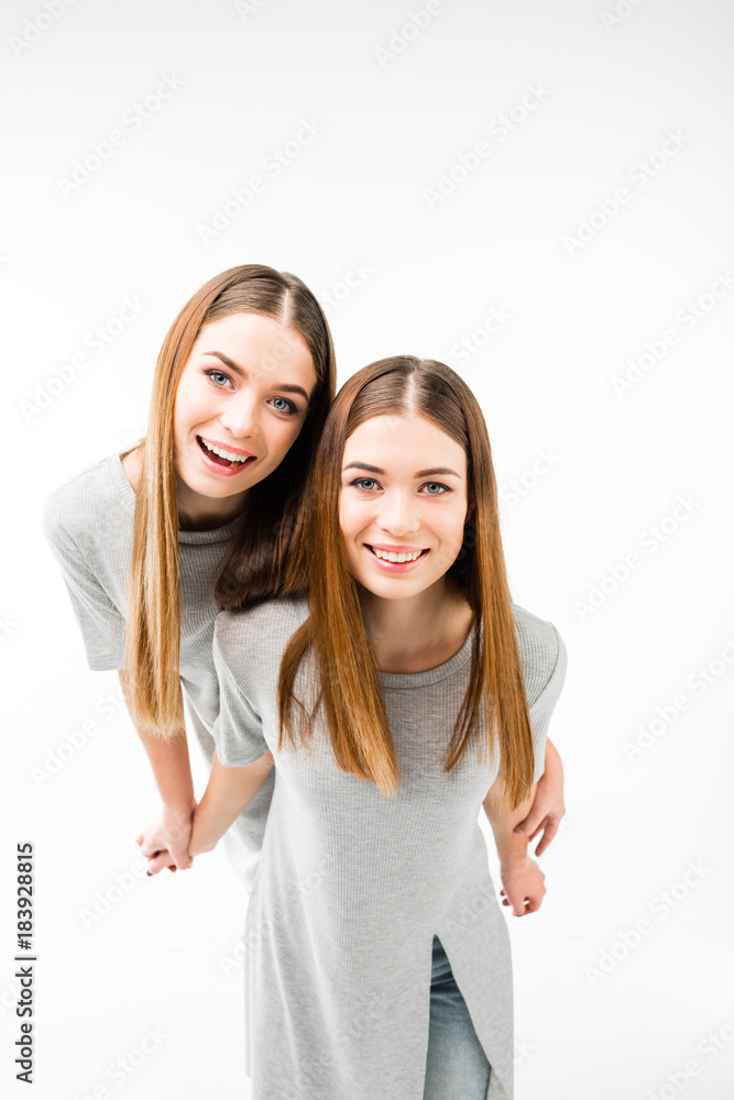 portrait of happy twins in grey tshirts holding hands and looking at camera isolated on white portrait of happy twins in grey tshirts holding hands and looking at camera isolated on white