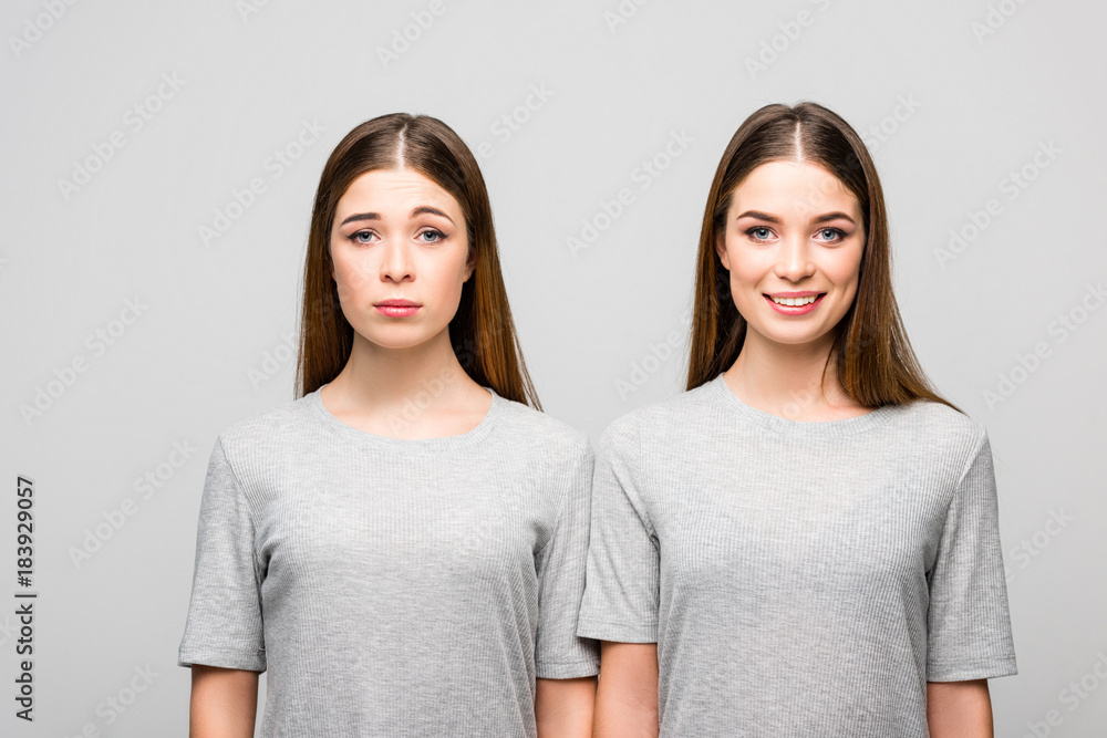 portrait of twin sisters in grey tshirts showing emotions isolated on grey portrait of twin sisters in grey tshirts showing emotions isolated on grey