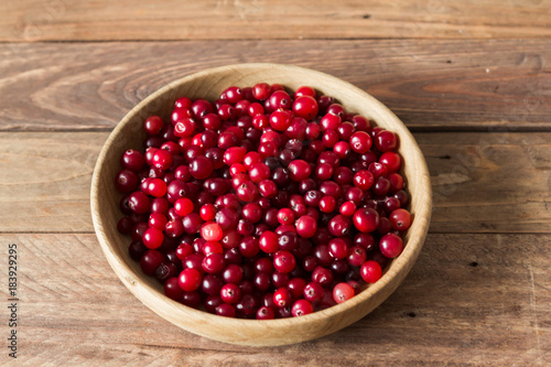 Red berries in a wooden plate on a wooden background with spruce branches. Cranberry.