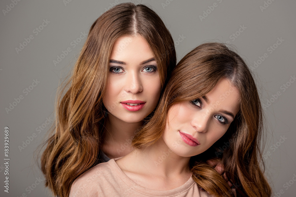 portrait of beautiful twin sisters with bright makeup looking at camera isolated on grey portrait of beautiful twin sisters with bright makeup looking at camera isolated on grey