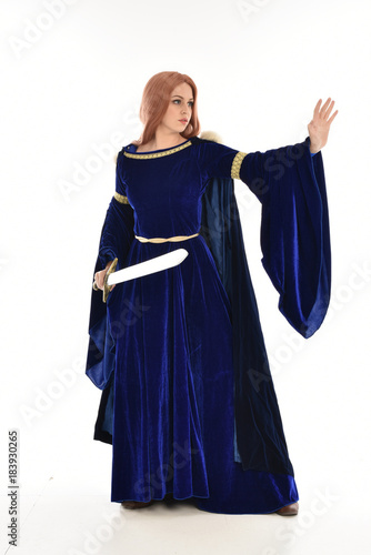  full length portrait of girl wearing long blue velvet gown and fur lined cloak, standing pose on white background.