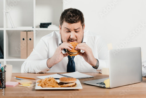 Photos overweight businessman eating junk food in office