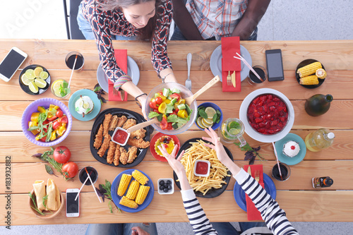 Top view of group of people having dinner together while sitting at wooden table. Food on the table. People eat fast food.