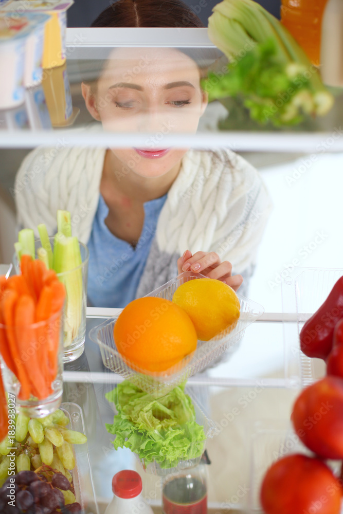 Portrait of female standing near open fridge full of healthy food, vegetables and fruits. Portrait of female Portrait of female standing near open fridge full of healthy food, vegetables and fruits. Portrait of female
