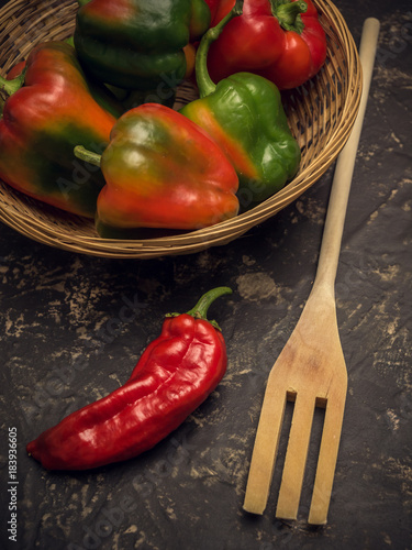 red pipper and wodden fork on stone table in kitchen, with basket of green peppers photo