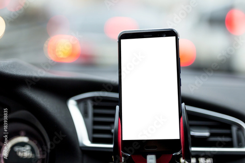 Smartphone or GPS device in a holder on car's dashboard with blurred traffic jam on the background. Mock up white emty screen for text photo