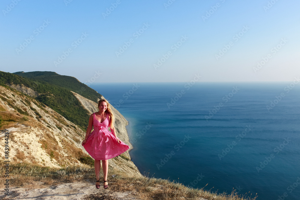 A girl in a pink dress jumps on the seashore and smiles. The joy of travel. Healthy lifestyle. Happiness and smile.