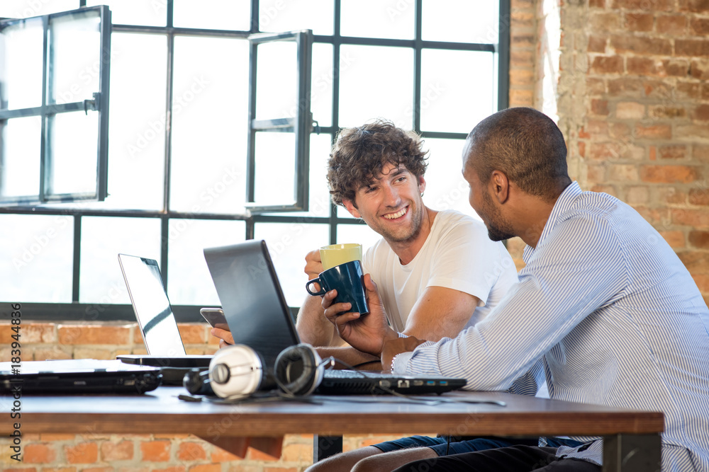 Two young businessmen working together in co-working space, using laptops Two young businessmen working together in co-working space, using laptops