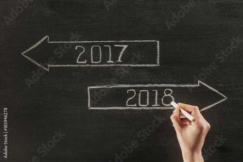 cropped shot of female hand with chalk and 2017, 2018 signs on dark wooden surface