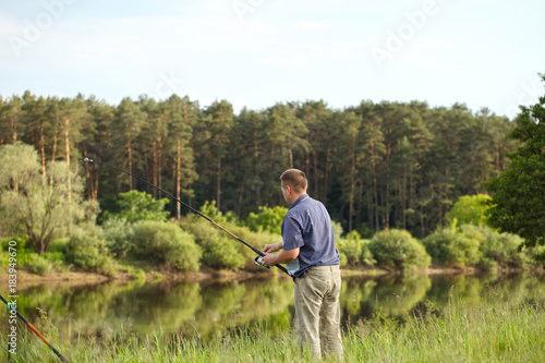 The fisherman is fishing on the bank of the river in a warm summer day. A man's hobby in nature.