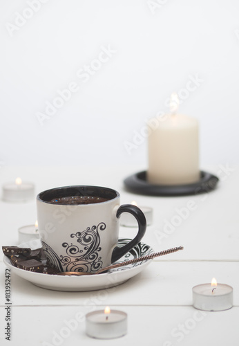 White cup with fresh coffee, spoon and candles.