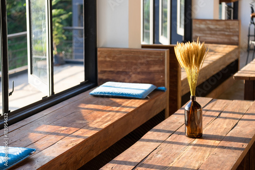 Relaxing area with wooded long chair and blue pillow near glass window, dry Flowers in a brown glass bottle on wooden table. copy space for text