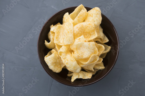 Potato chips with cheese in a plate that is located on a gray background.