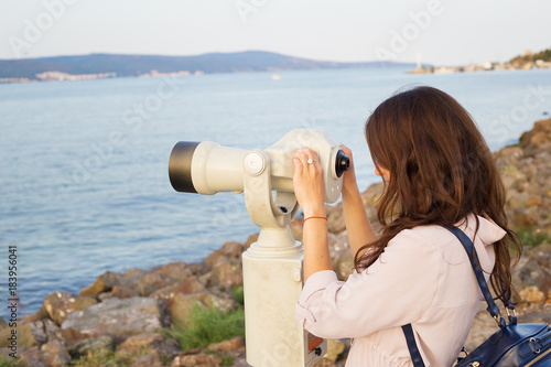 The girl looks through the telescope at the sea.