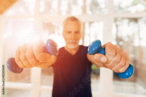 An elderly man is holding dumbbells in his hands in a nursing home.