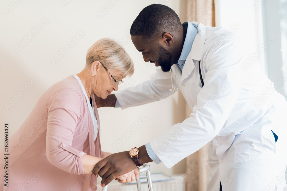 The doctor helps to get out of bed an elderly woman in a nursing home. The doctor helps to get out of bed an elderly woman in a nursing home.