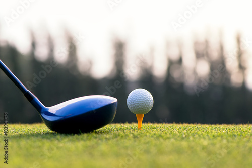Close up golf ball and driver, player doing golf swing tee off on the green sunset evening time, presumably does exercise, select focus. Healthy and Lifestyle Concept.