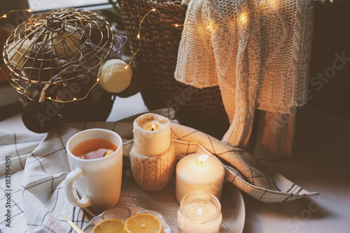 Cozy winter morning at home. Hot tea with lemon, candles, knitted sweaters in basket and modern metallic interior details. Still life composition, danish hygge concept photo