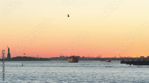 Real time New York Upper Bay footage at sunset in New York. Helicopters, aircrafts, ferris and yachts are making busy traffic. Iconic Statue of Liberty in the left corner.