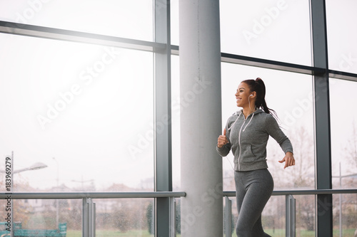 Fit sporty girl running indoors on rainy day.