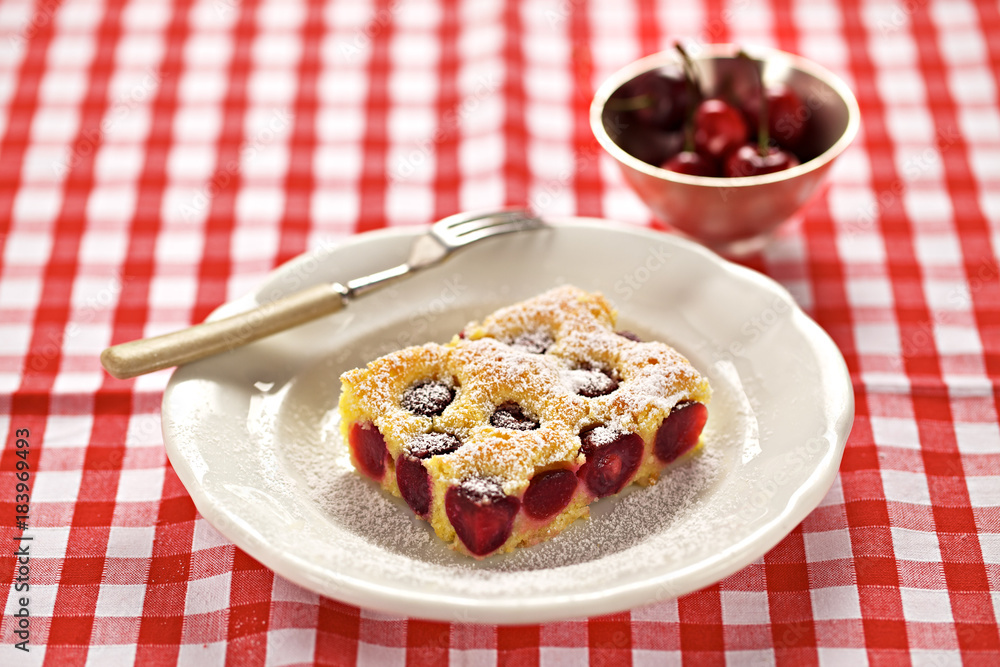 Ein Stück Kirschkuchen auf einer rot-karierten Tischdecke und eine Schale mit frischen Kirschen Ein Stück Kirschkuchen auf einer rot-karierten Tischdecke und eine Schale mit frischen Kirschen