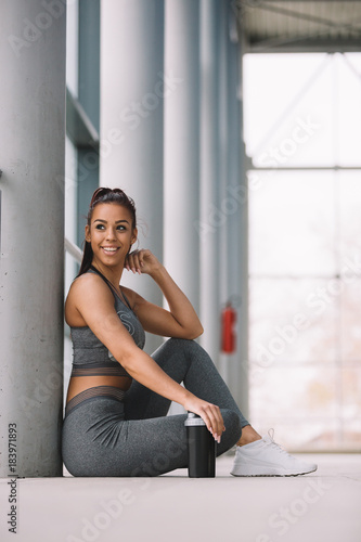 Fit sporty girl siting on floor and holding her shaker