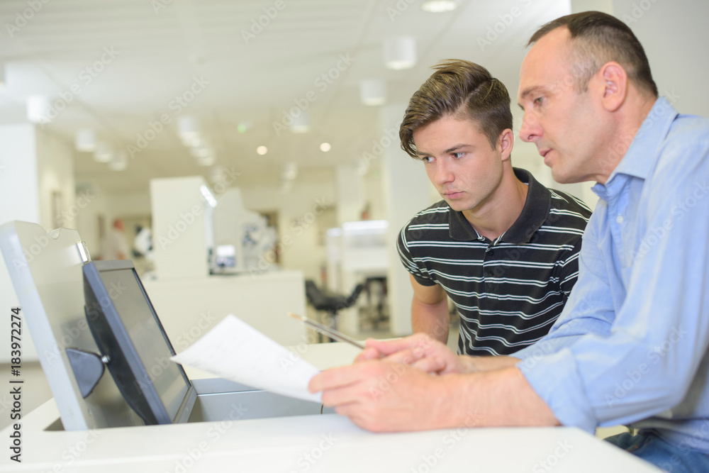 Two men looking at paperwork and equipment Two men looking at paperwork and equipment