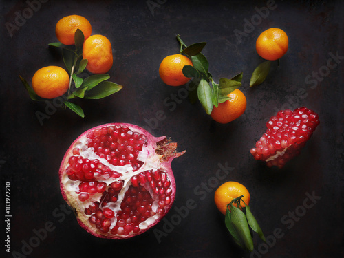A composition of pomegranate in a cut and tangerines with leaves on a dark metallic background. Top view, flat lay.