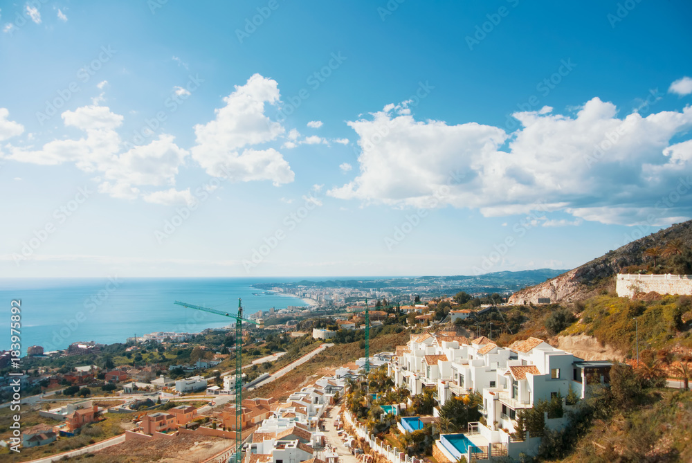 A view from the viewpoint over the hill near The Buddhist Stupa in Benalmadena town to white houses and constructional cranes, Fuengirola and Mediterranean sea at the background.