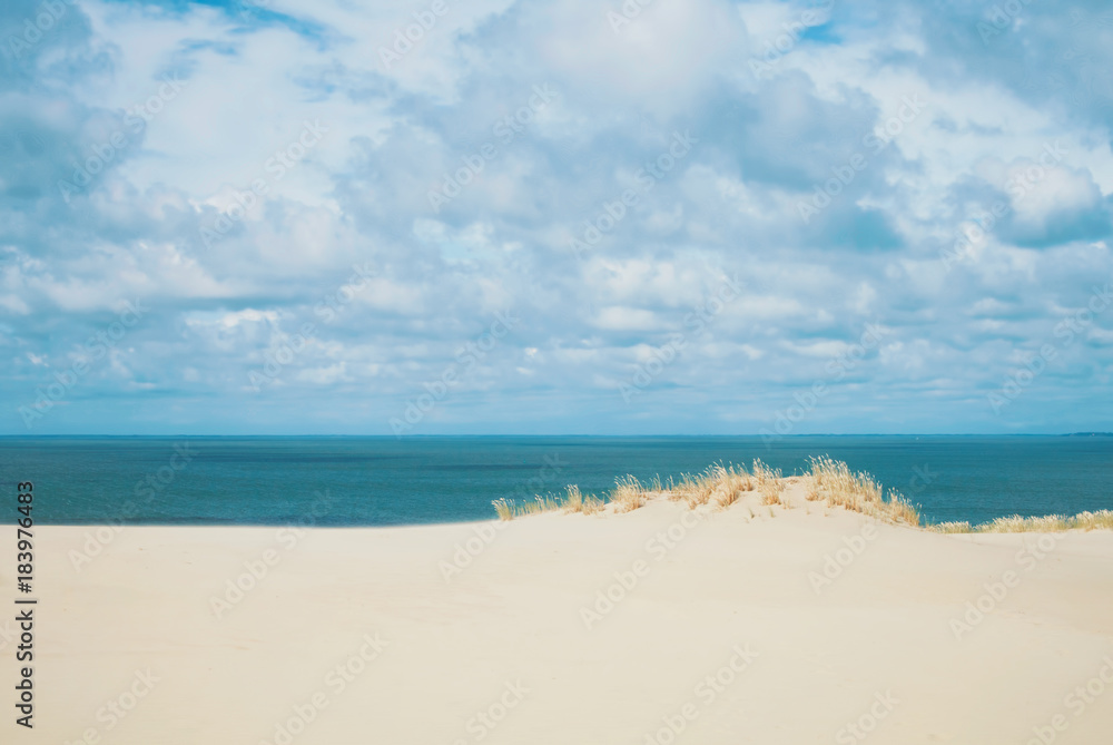 Sand dunes covered with dry grass and blue Baltic sea water at the background national park of Curonian Spit, Lithuania on summer cloudy day.