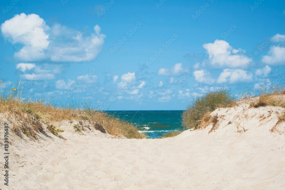 Sand dunes covered with dry grass and blue Baltic sea water at the background national park of Curonian Spit, Lithuania on summer cloudy day. Sand dunes covered with dry grass and blue Baltic sea water at the background national park of Curonian Spit, Lithuania on summer cloudy day.
