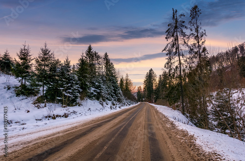 road through winter forest at dusk. lovely transportation scenery in mountains with snowy hills