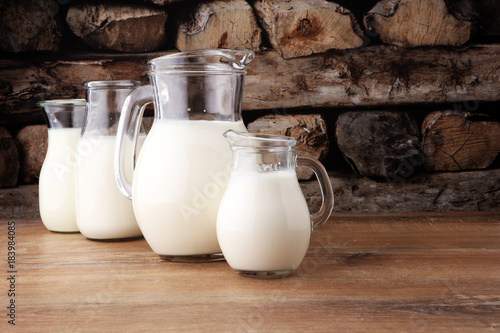 A jug of milk and glass of milk on a wooden table.