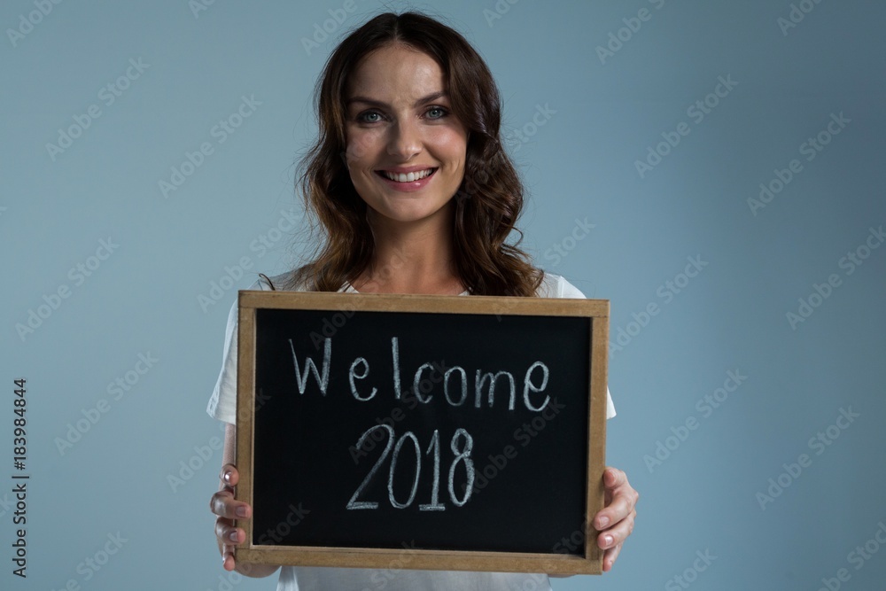 Smiling woman showing slate with text welcome 2018 against grey