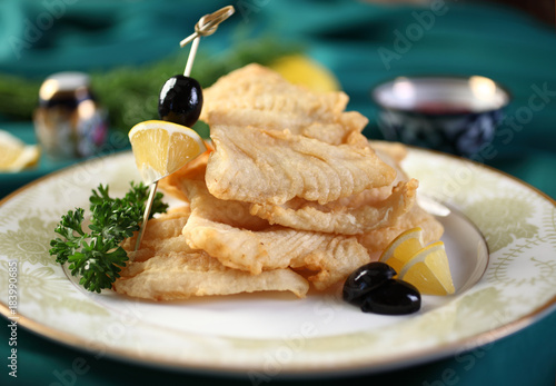 Fried walleye on a plate with lemon and olives.Selective focus.