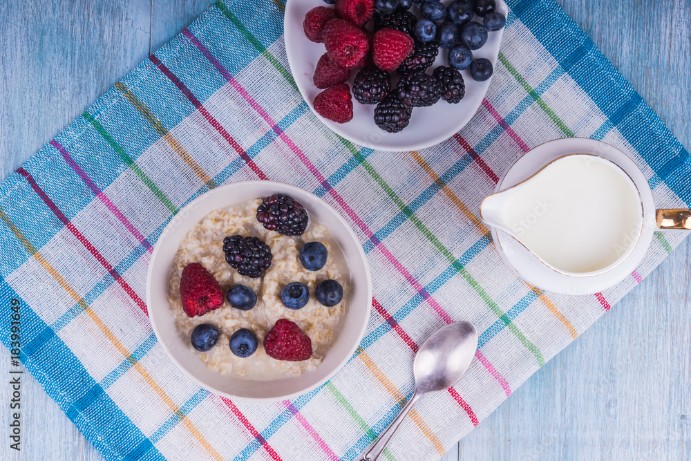 Oatmeal porridge with berries and milk on a rustic wooden background - a healthy organic breakfast Oatmeal porridge with berries and milk on a rustic wooden background - a healthy organic breakfast