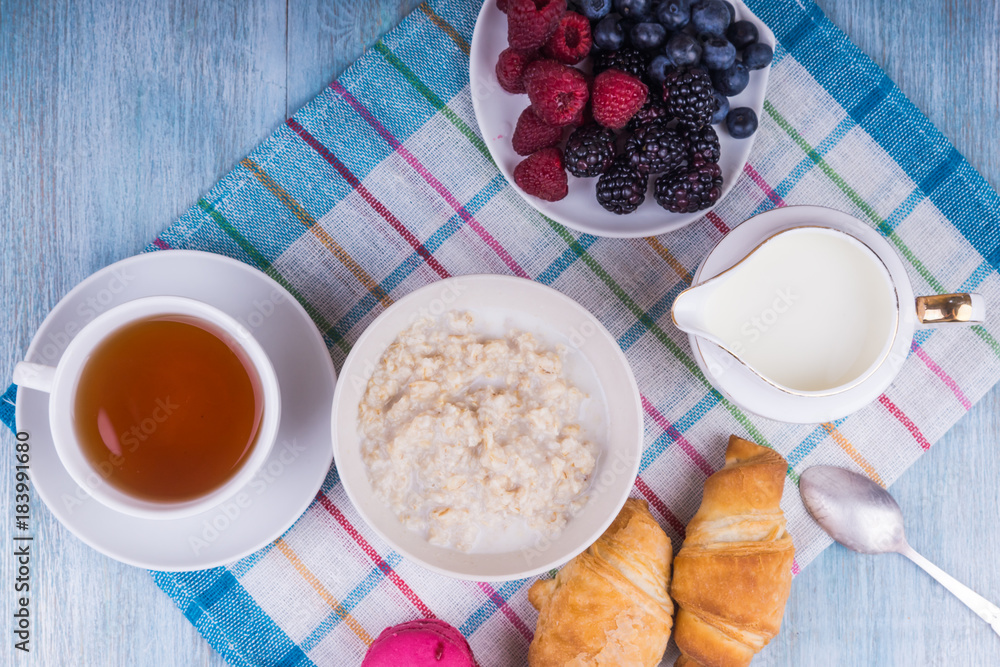 Organic vegetarian breakfast - oatmeal with berries, milk, tea and croissants Organic vegetarian breakfast - oatmeal with berries, milk, tea and croissants