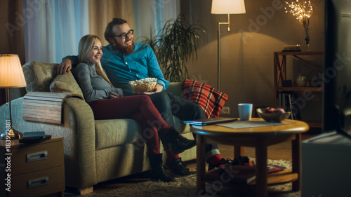 Obraz na plátně In the Evening Man and Woman are Sitting on the Sofa Watching TV and Eating Popcorn