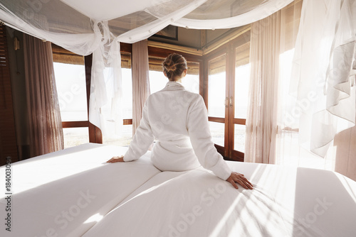 Young woman in a bathrobe watching the sunrise from her hotel bed photo